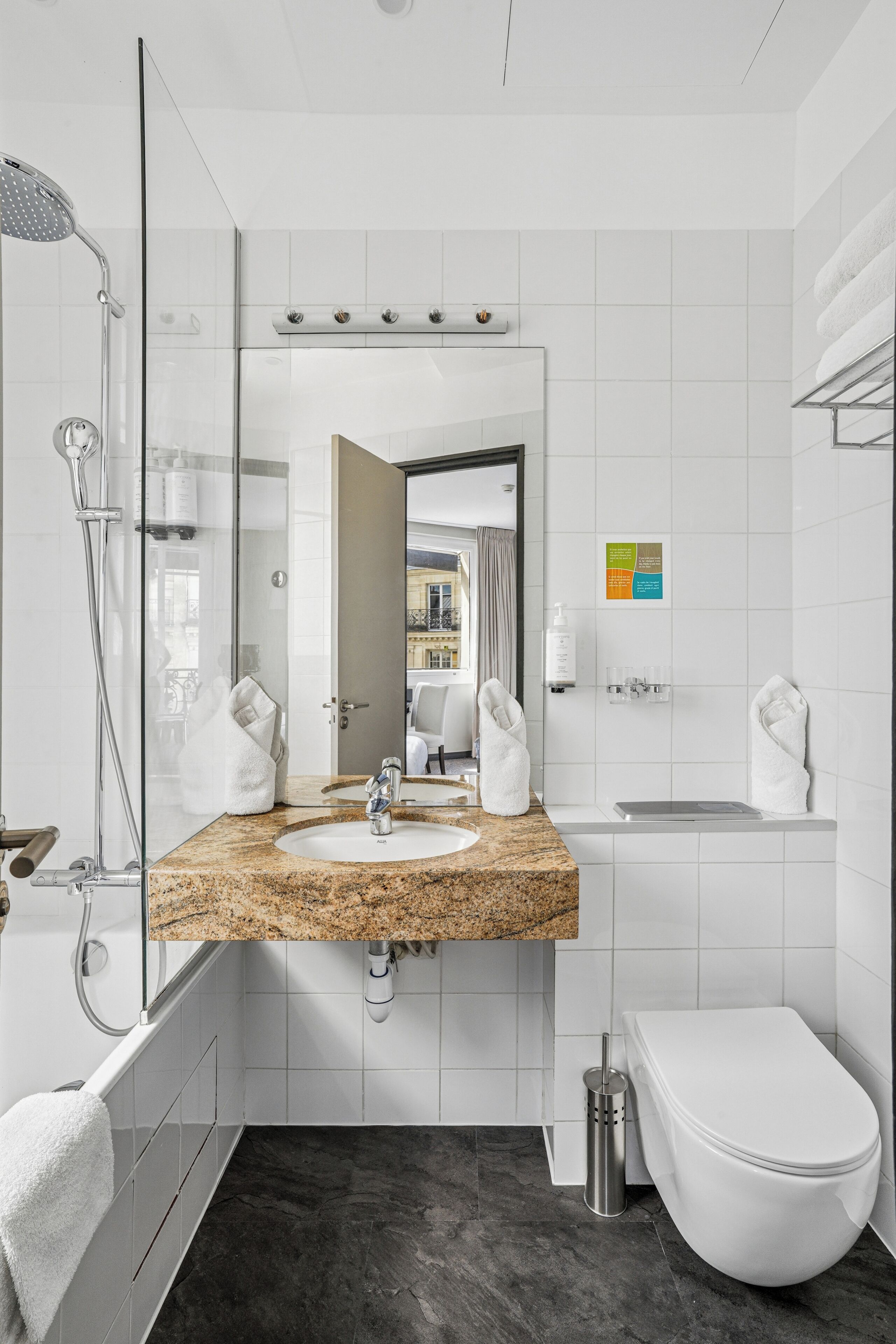 A modern bathroom with a glass shower enclosure, a granite countertop sink, a white toilet, and a mirror reflecting the room.