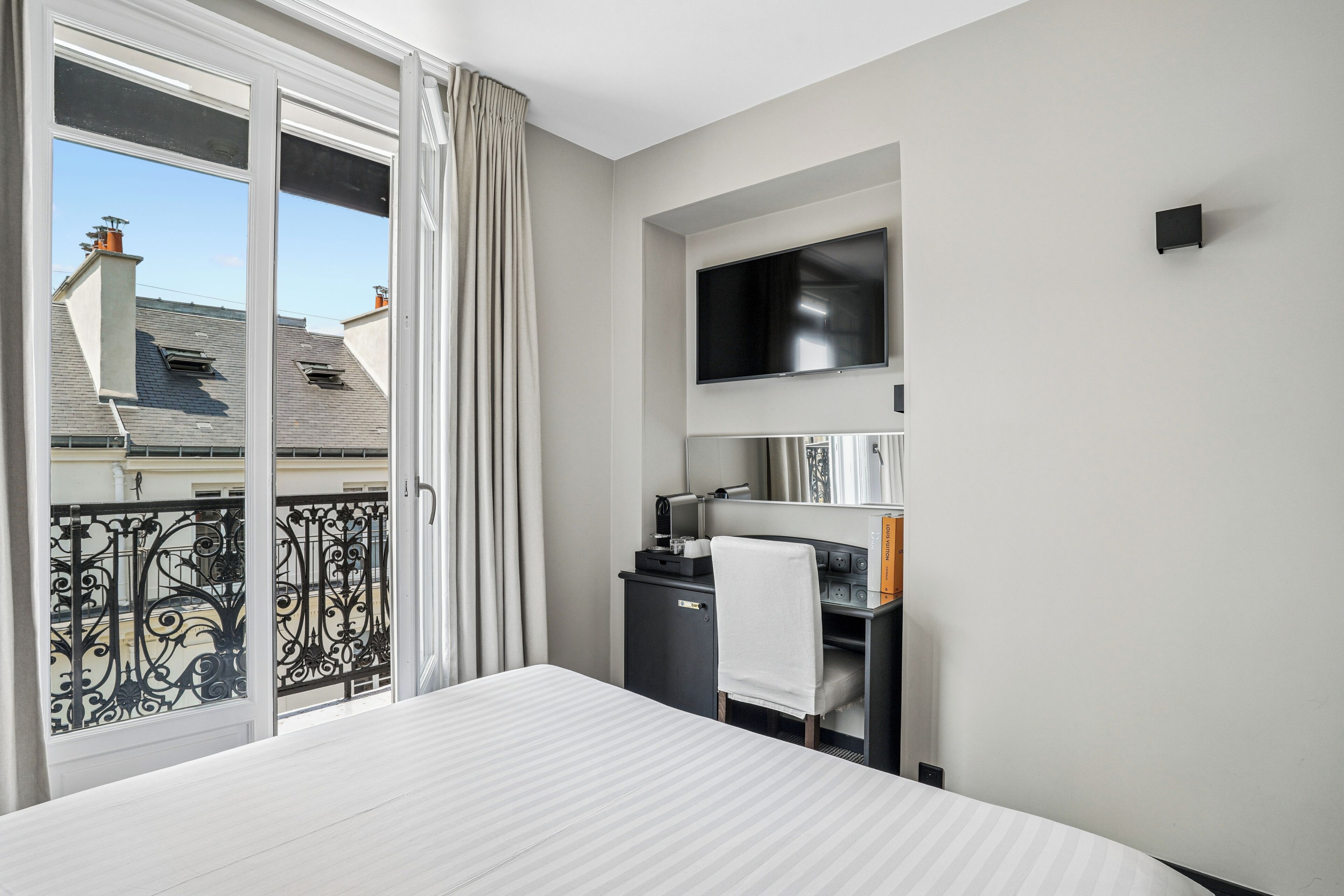 A hotel room with a bed, a desk with a chair, a flat-screen TV, and a sliding glass door to the outside.