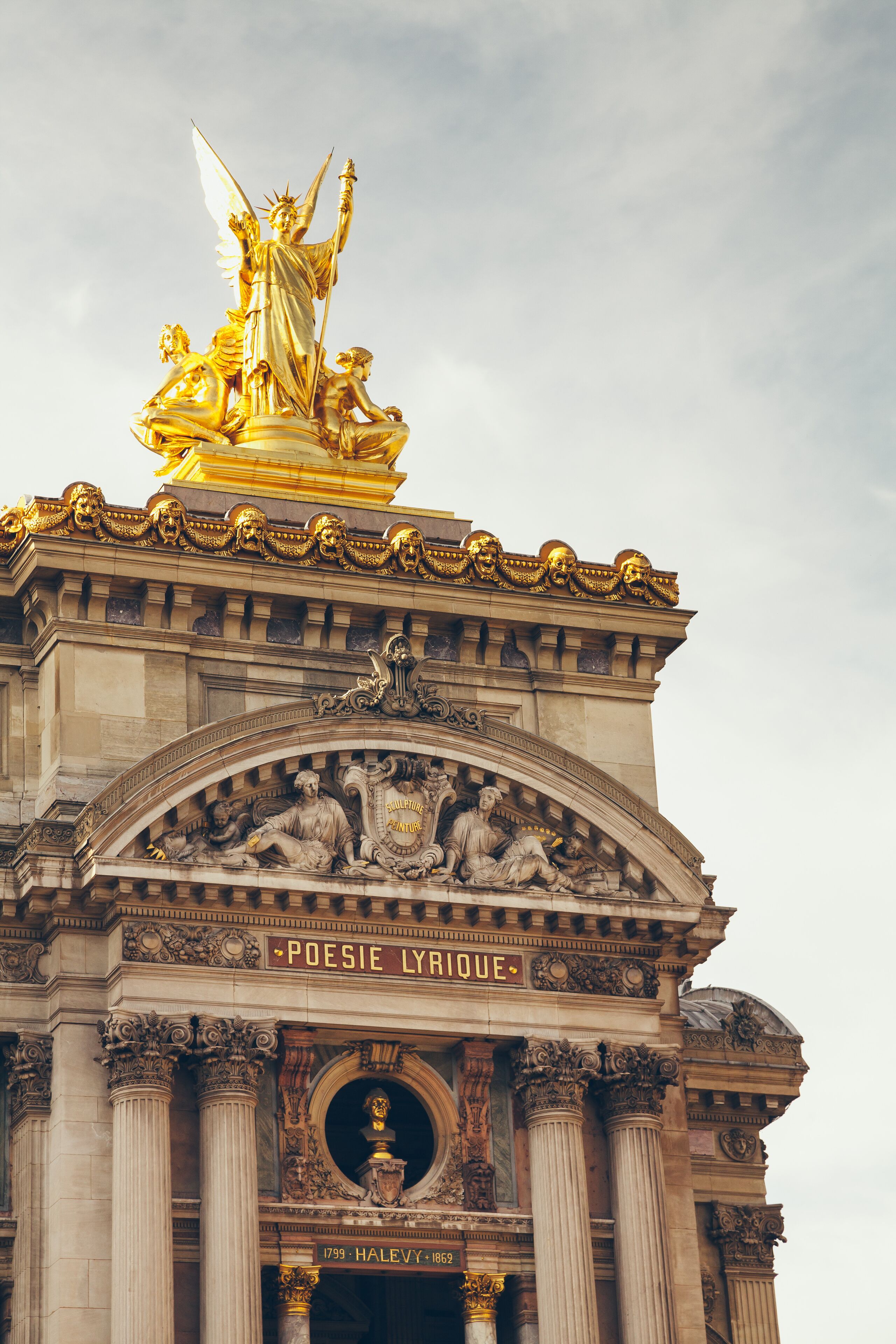 A grand entrance with a statue of a woman holding a torch, columns, and intricate carvings.
