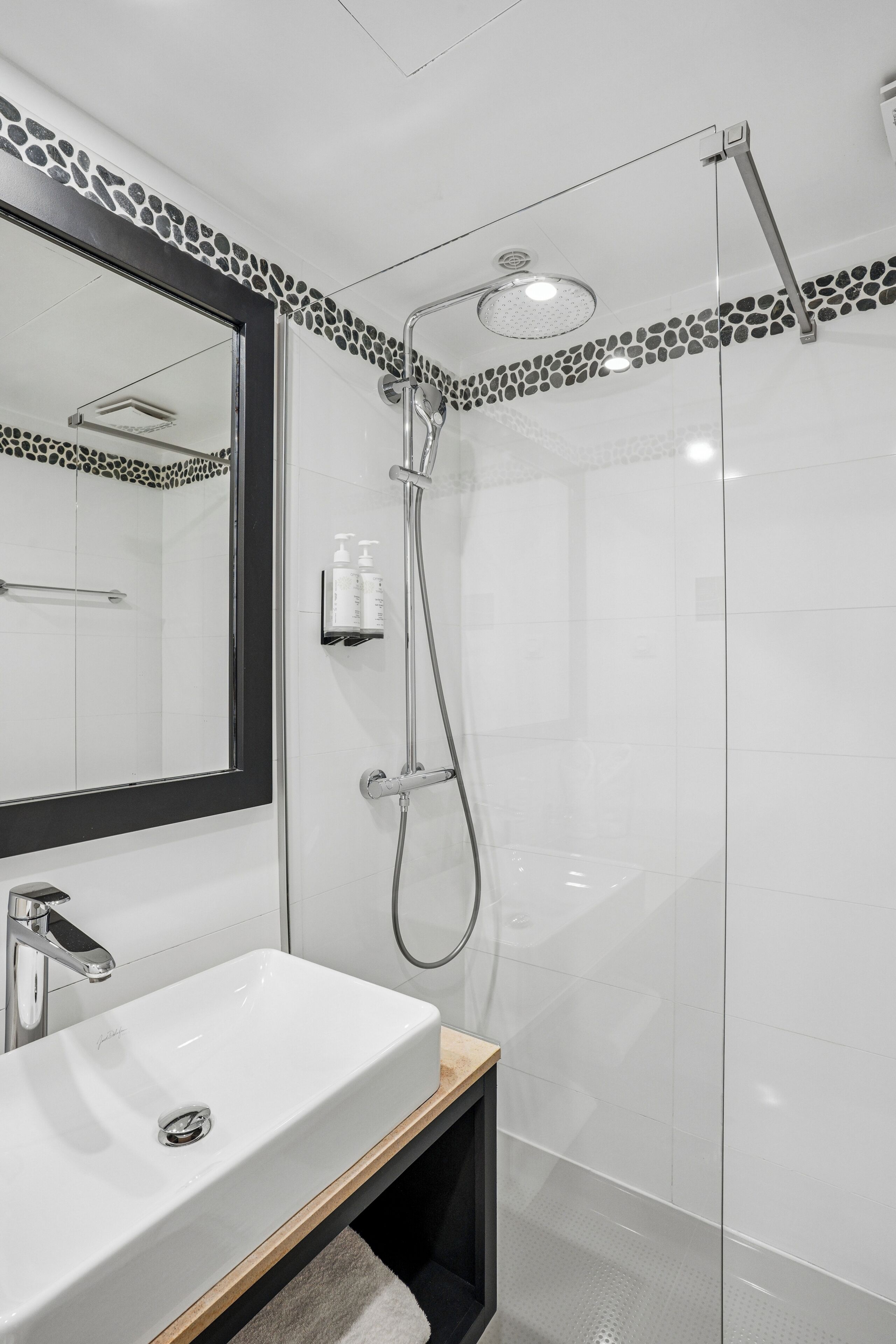 Un baño moderno con un lavamanos blanco, una ducha con cerramiento de vidrio y un espejo con marco negro.