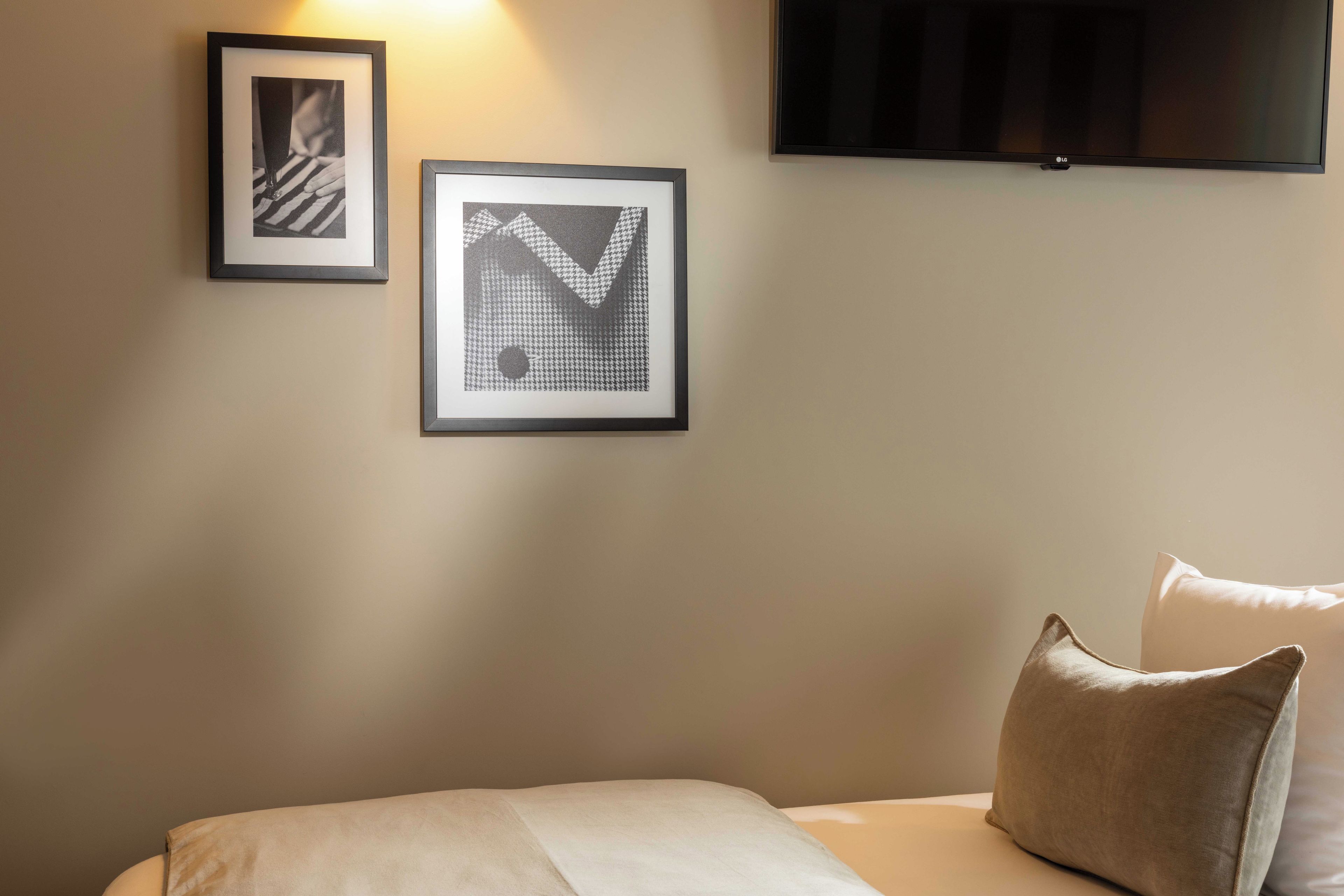 Een hotelkamer met een bed, twee ingelijste foto's aan de muur en een flatscreen televisie boven het bed.