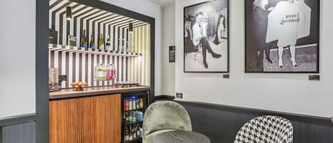 A bar area with a striped back wall, a refrigerator stocked with beverages, and a seating area with patterned chairs.