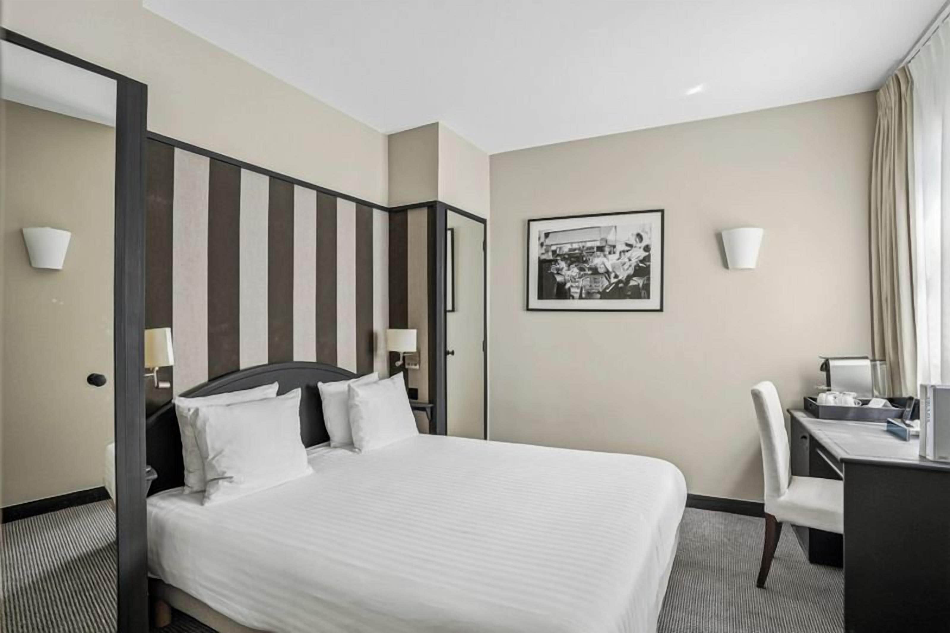 Una habitación de hotel con una cama grande, un escritorio, una silla y un cuadro en la pared.
