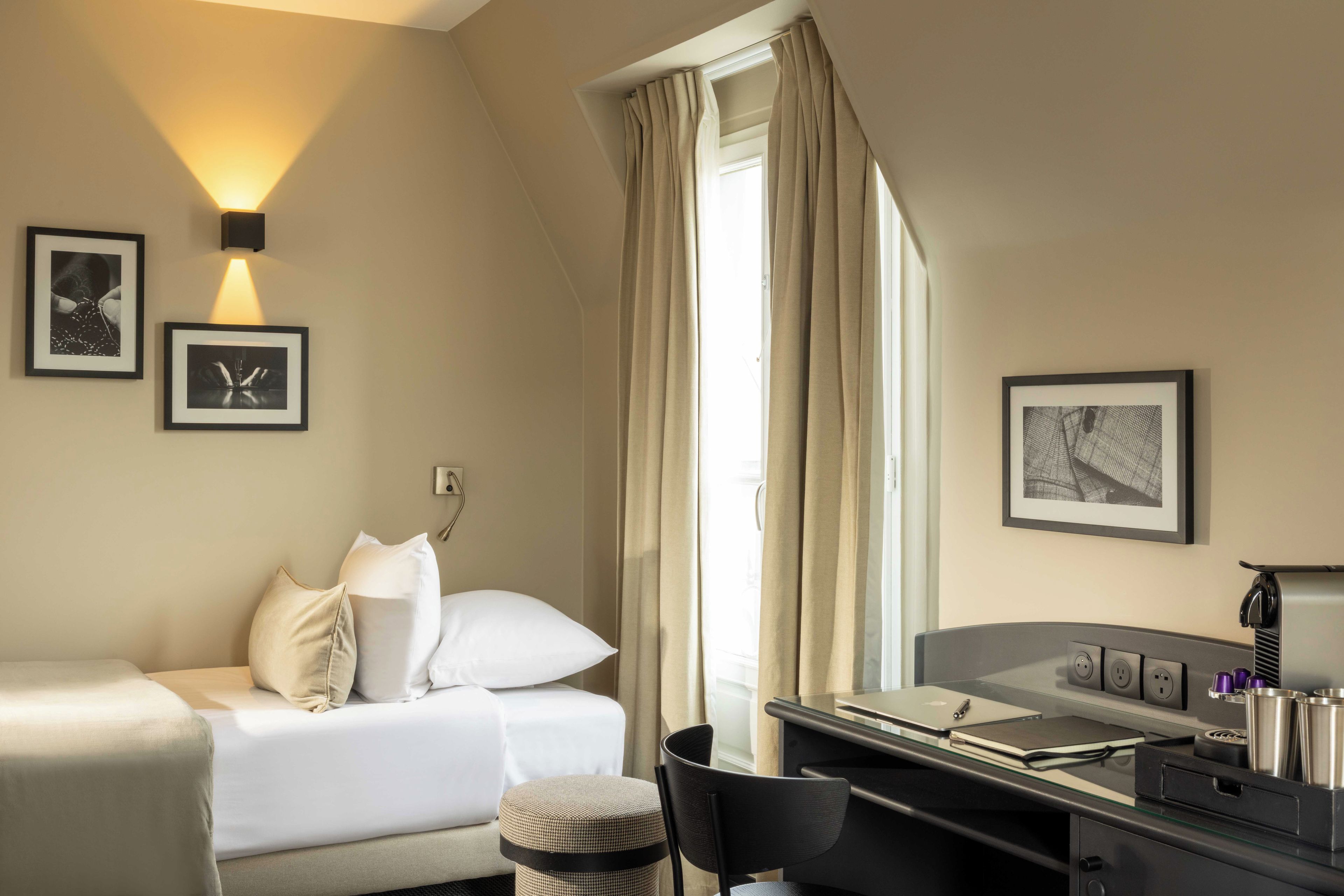A hotel room with a bed, a desk with a laptop, a chair, and a window with curtains.
