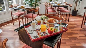 A breakfast tray with food and drinks, wooden chairs, and a view of the dining area. - Hôtel Excelsior Opéra (Paris)