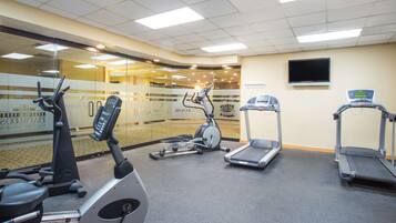 Une salle de sport équipée de vélos d’appartement, de tapis de course et d’un mur recouvert de miroirs.