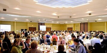 Un salón de conferencias amplio con varias mesas y asistentes.