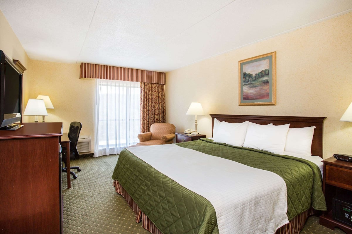 A hotel room with a large bed, two bedside lamps, a desk with a computer, a chair, and a painting on the wall.