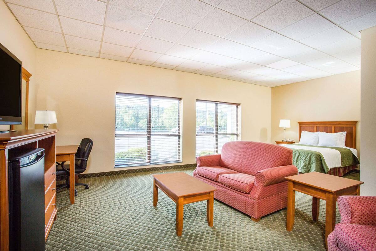 A hotel room with a bed, two armchairs, a desk, a television, and a dresser.