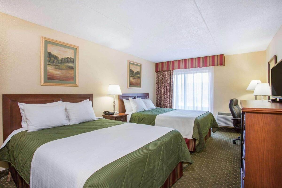 A hotel room with two beds, a desk, a chair, a TV, and a window with curtains.