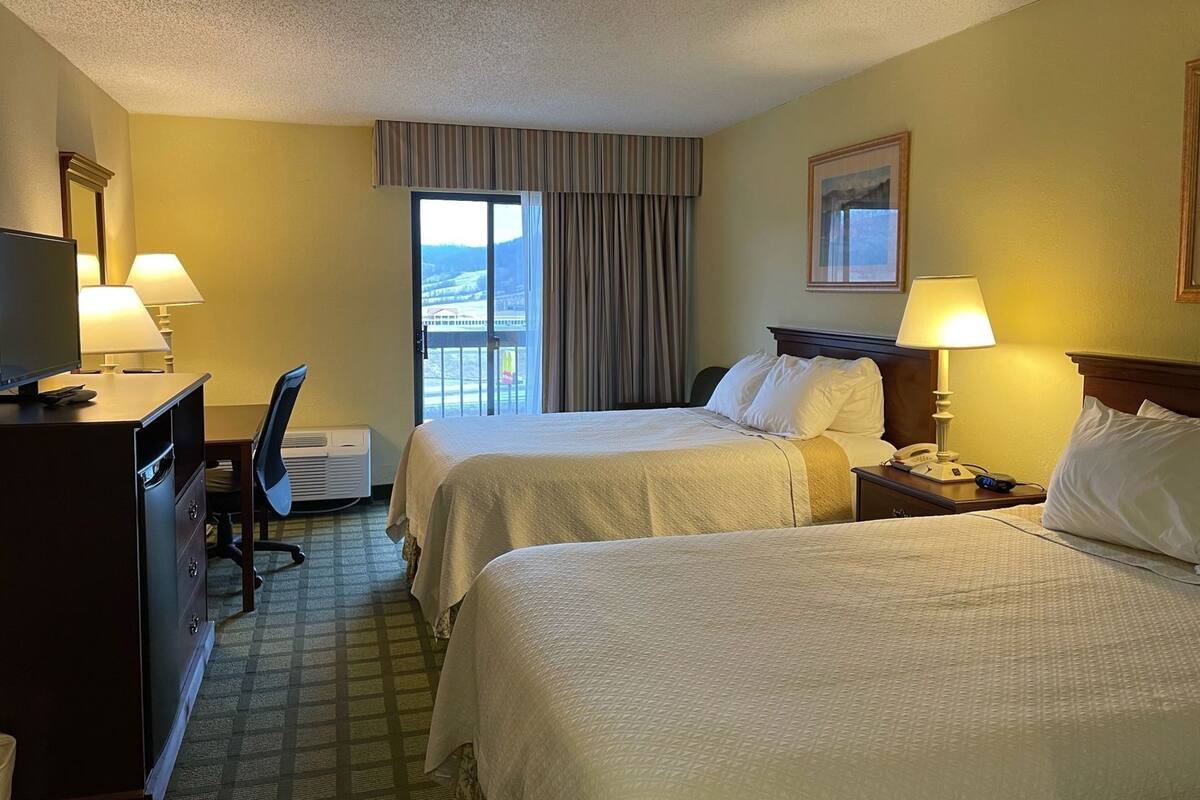A hotel room with two beds, a desk with a chair, a television, and a window with curtains.