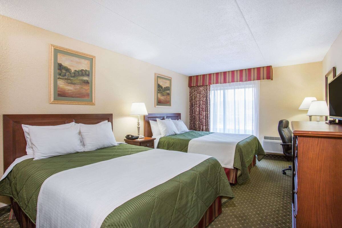 A hotel room with two beds, a desk, a chair, and a television.