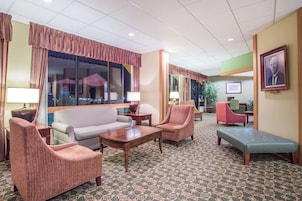 Un hall de hotel con alfombra estampada, un sofá, sillones, una mesita y un banco.