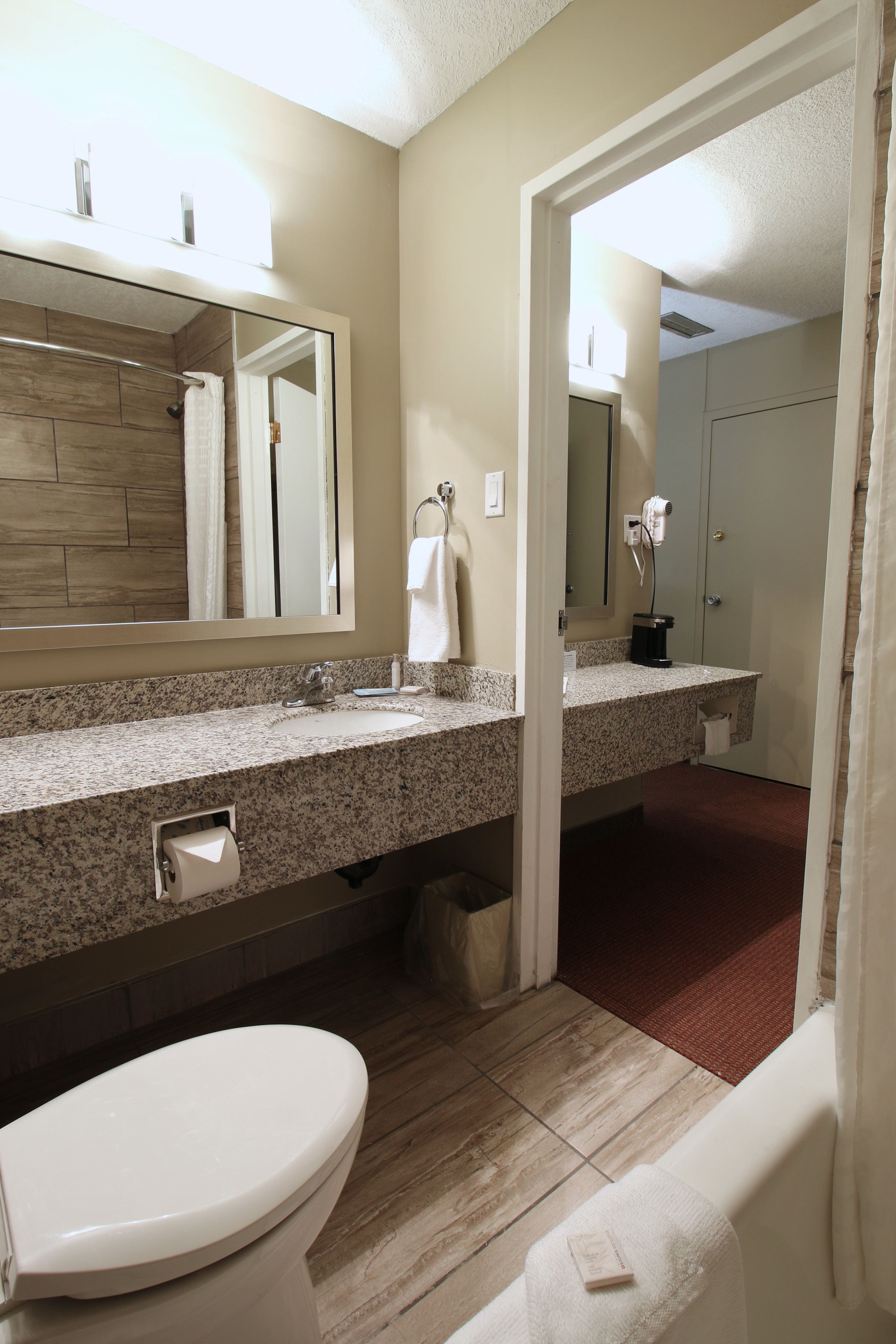 A bathroom with a toilet, sink, and mirror. There is a towel hanging on the wall and a shower visible in the background.