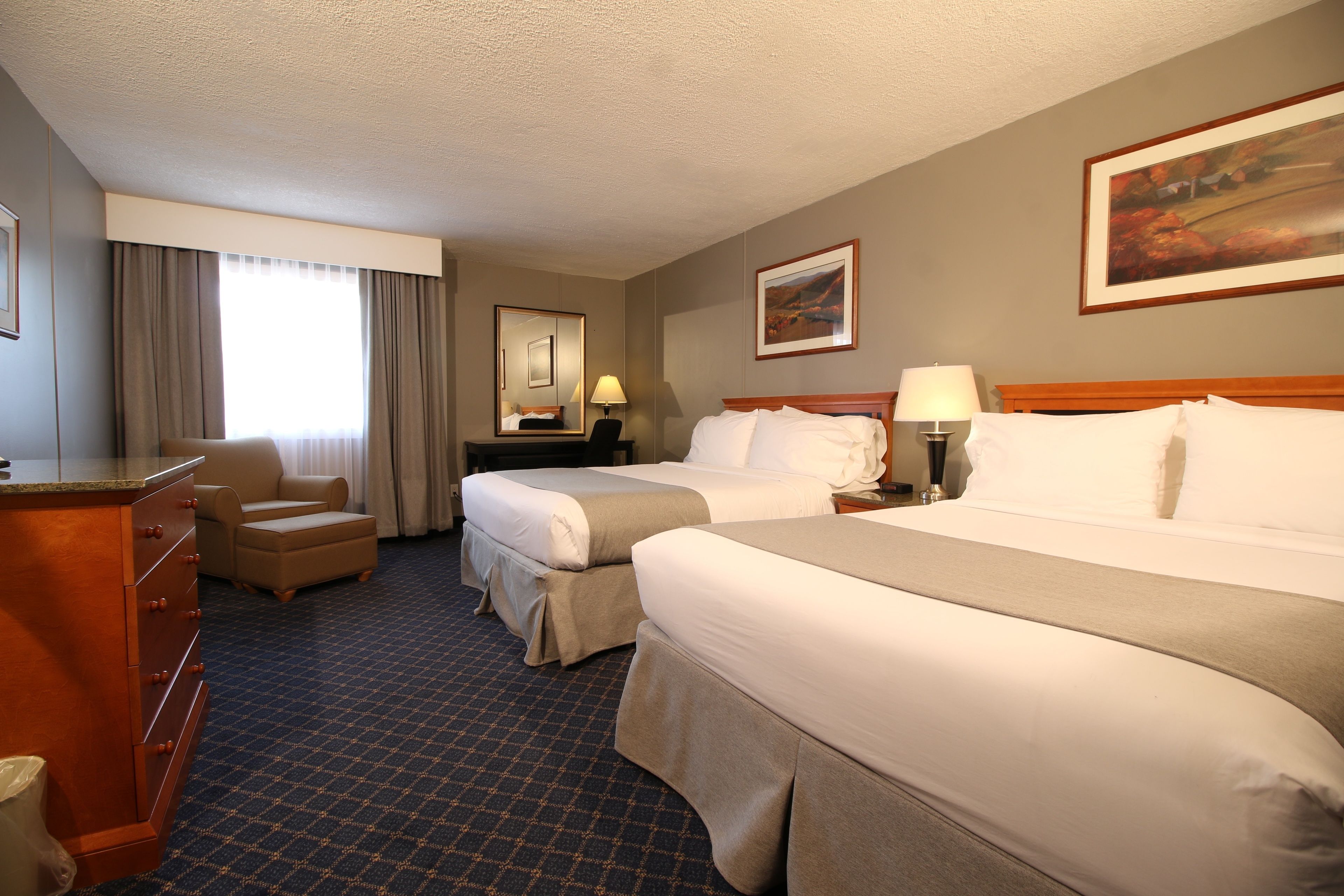 A hotel room with two beds, a desk, a chair, and a large window with curtains.