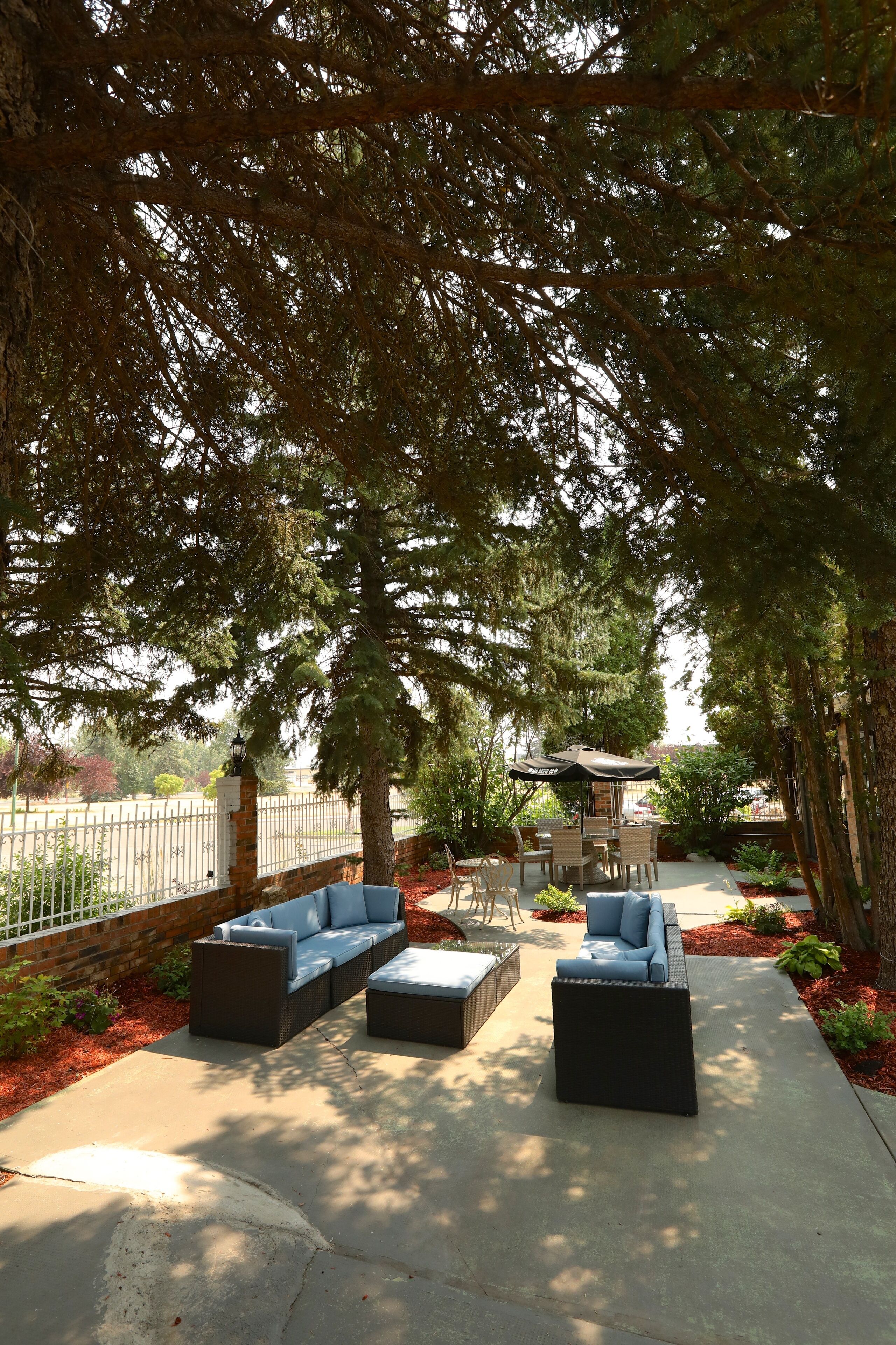 An outdoor patio area with a sofa set and a table, surrounded by trees and a brick wall.