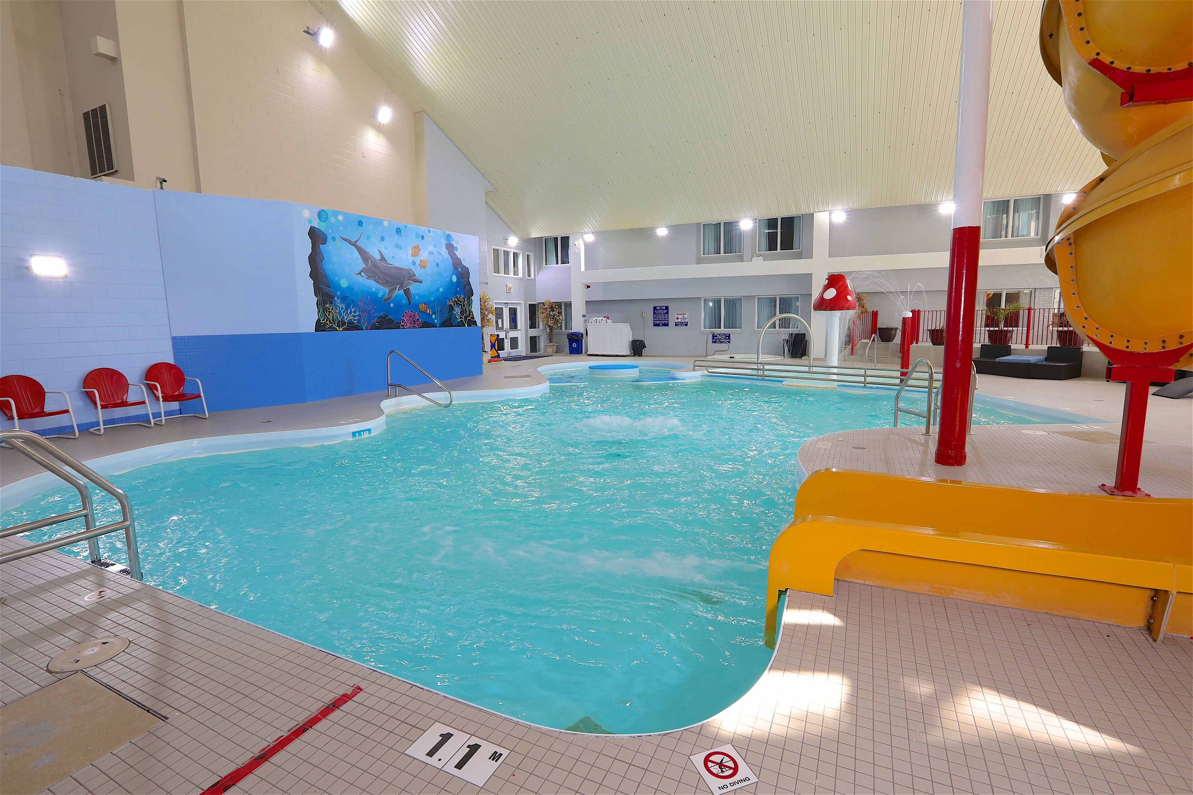 Une piscine intérieure dotée d’un plongeoir, d’une plateforme pour les sauveteurs et d’une fresque représentant un paysage sous-marin.
