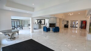 A spacious lobby with a marble floor, a round table, blue armchairs, and a stone fireplace. - Clarion Pointe Medicine Hat Saamis Tepee (Medicine Hat)
