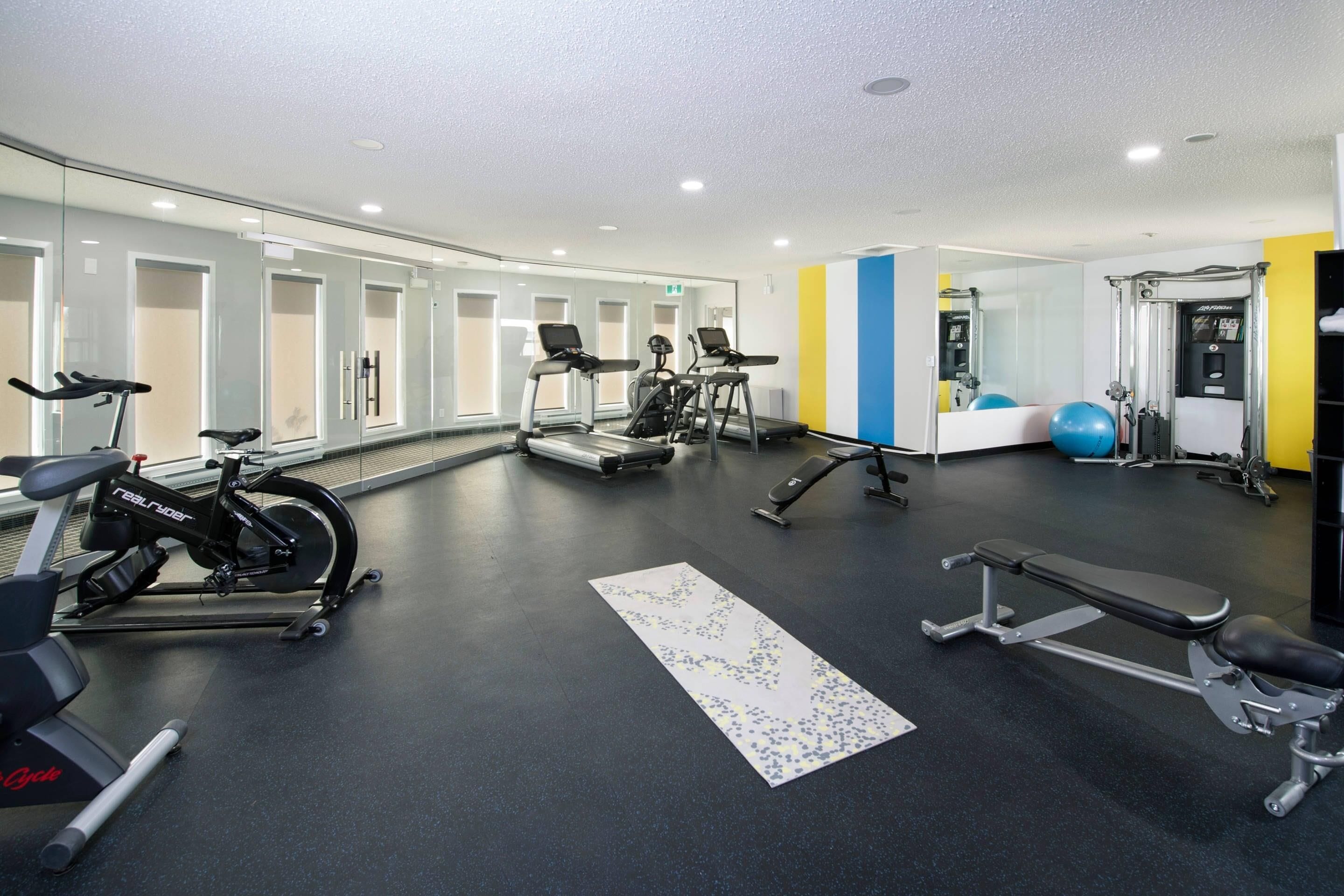 A gym with exercise equipment, a bench, and a mirrored wall.