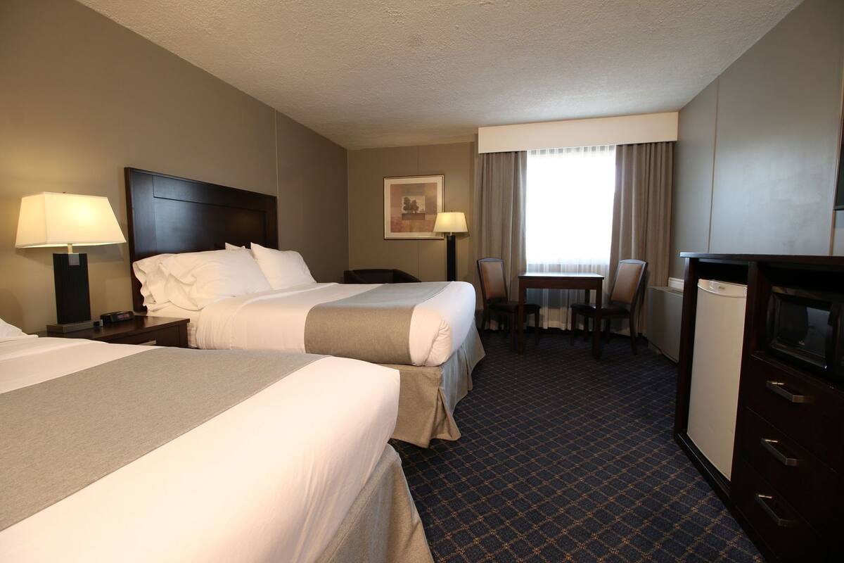 Habitación de hotel con dos camas, un escritorio, una silla, un televisor y una ventana con cortinas.