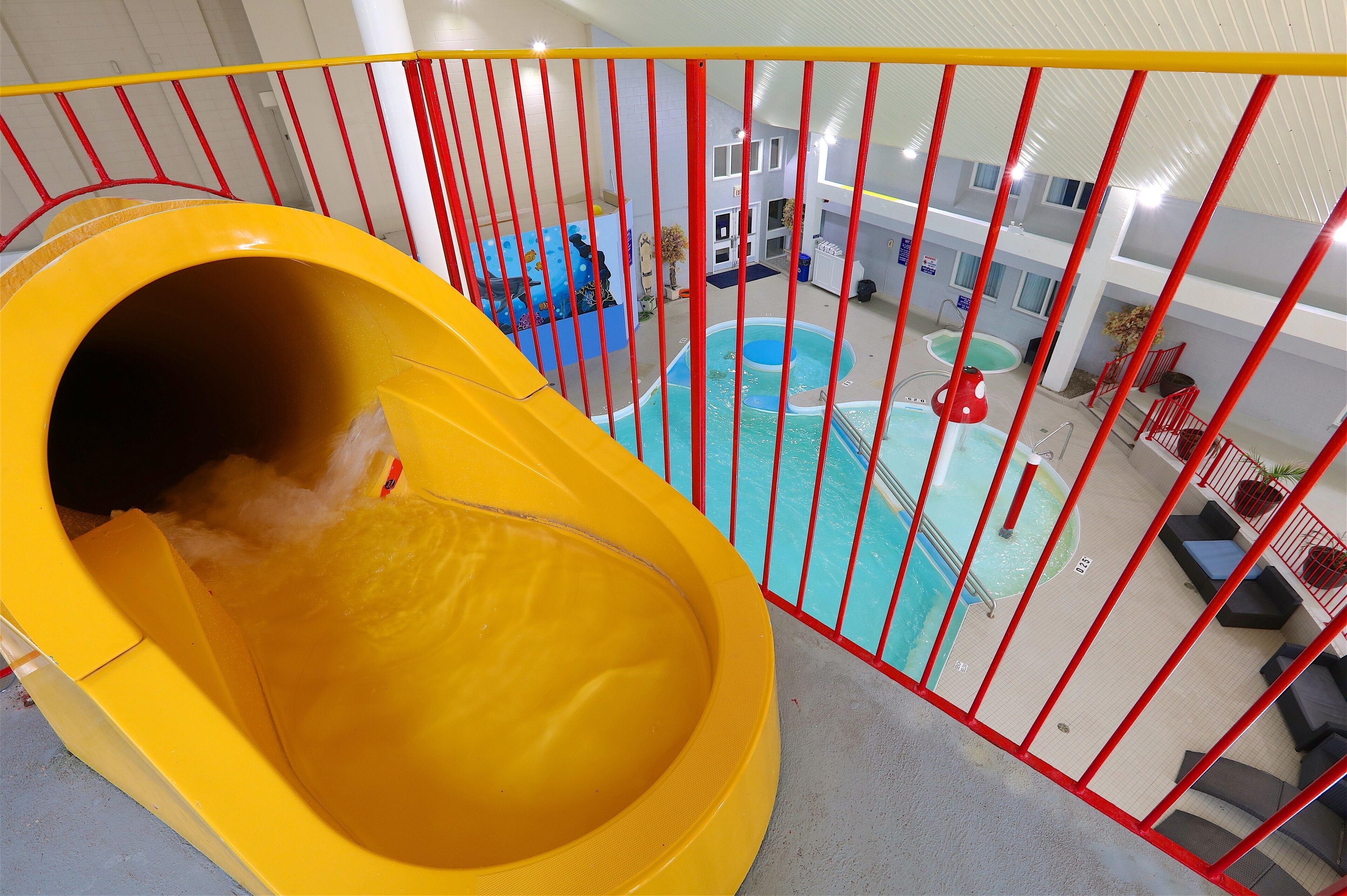 Un tobogán de agua interior amarillo que lleva a una piscina con barandillas rojas y vistas del interior del hotel.