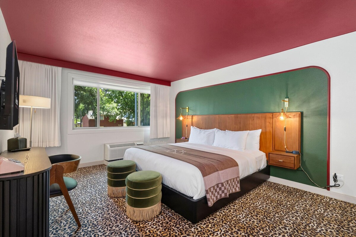 Une chambre d’hôtel avec un lit, un bureau, une chaise, une fenêtre et un tapis à motifs léopard.