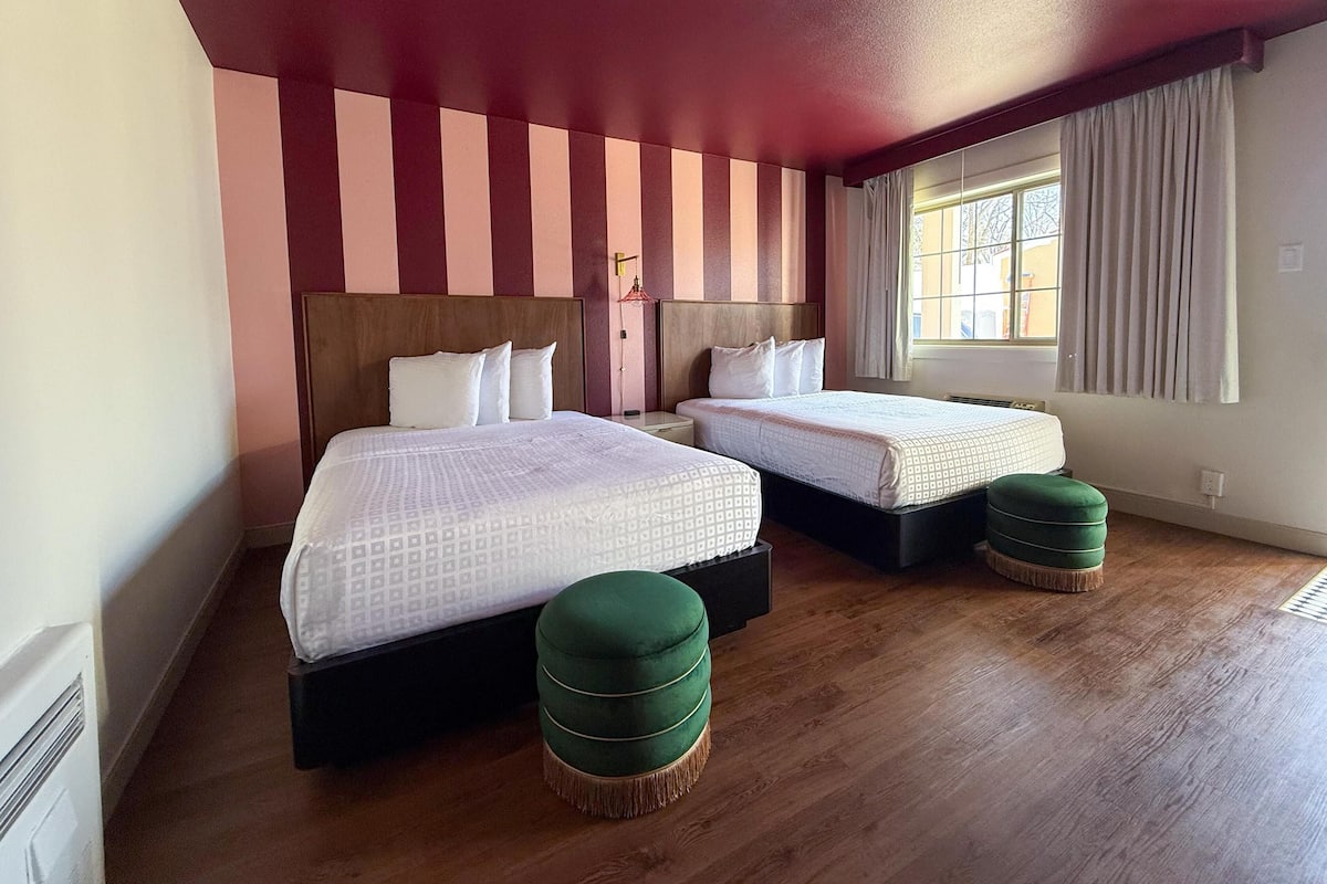 Une chambre d’hôtel avec deux lits, un plancher en bois, un mur à rayures et une fenêtre avec des rideaux.