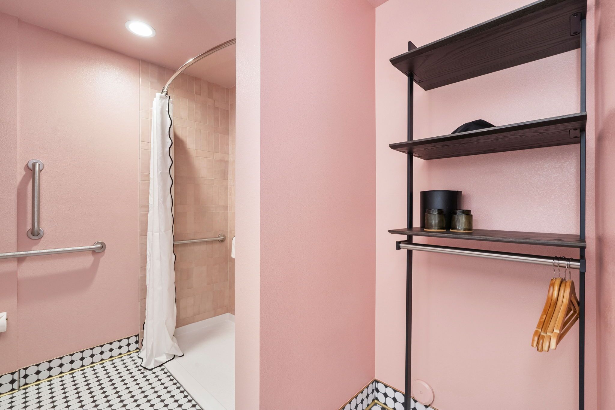 A bathroom with a shower, a handrail, a shelf with toiletries, and a towel rack.