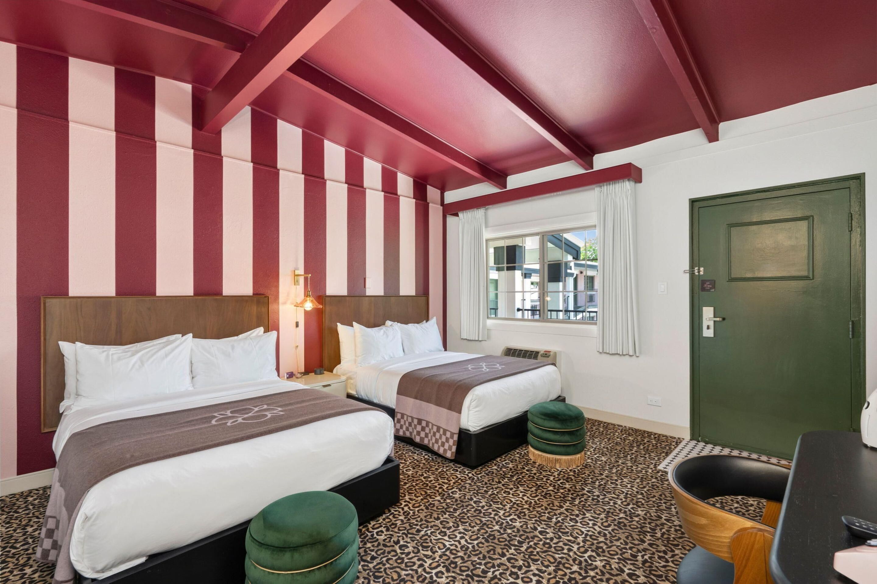 A hotel room with two beds, a green door, a window with curtains, and a leopard print carpet.