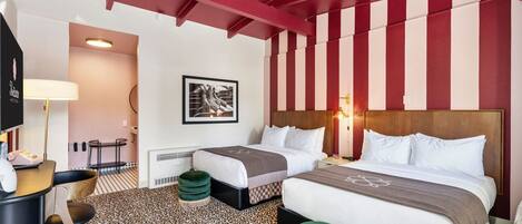 A hotel room with two beds, a desk, a chair, a lamp, a framed picture, and a patterned carpet.