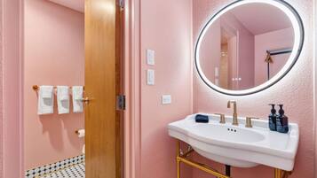 A bathroom with a white sink, gold fixtures, a round mirror, and a pink wall.
