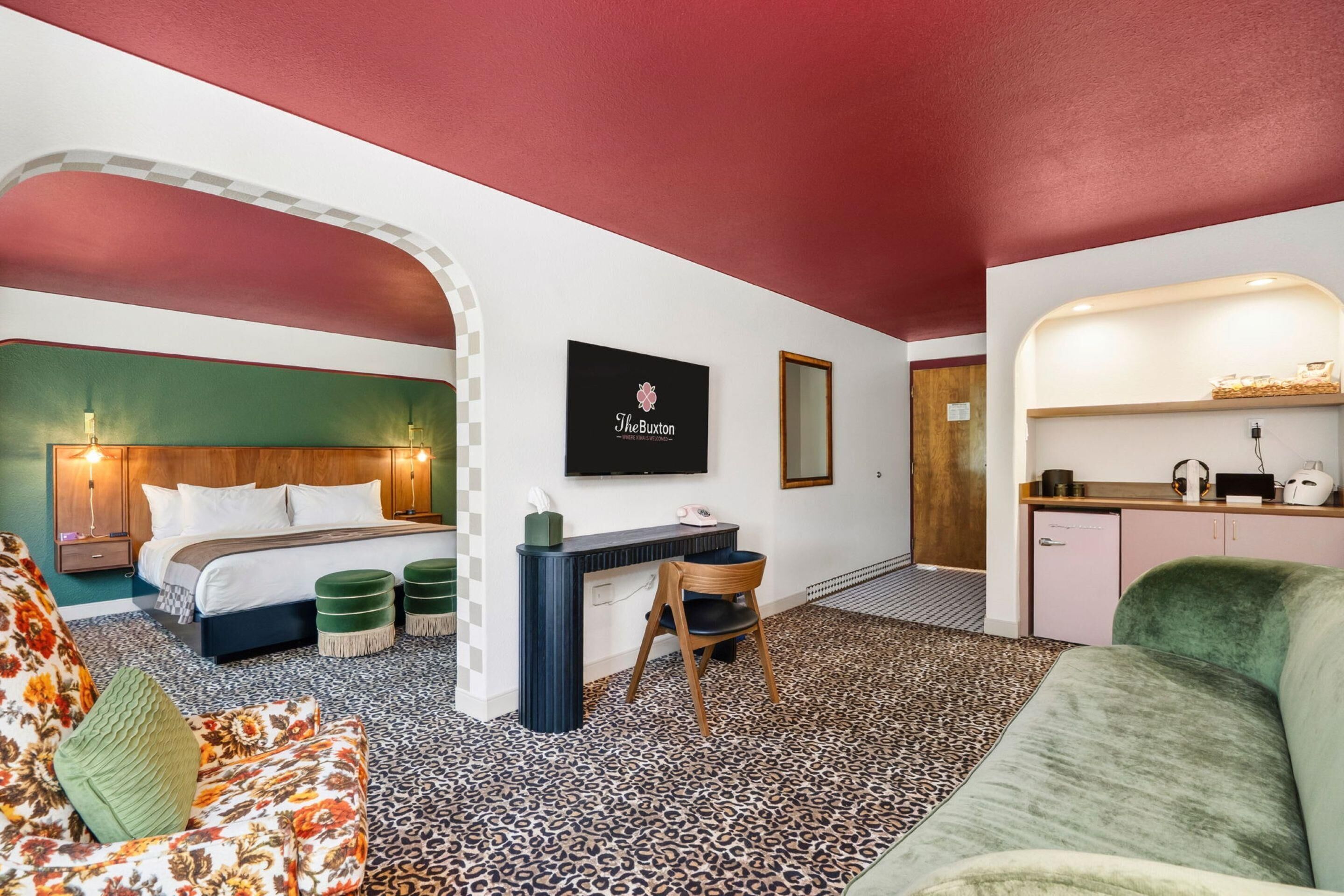 A hotel room with a bed, a desk, a chair, a sofa, and a kitchenette.