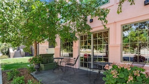 An outdoor patio with a table and chairs, a planter with flowers, and a building with large windows.