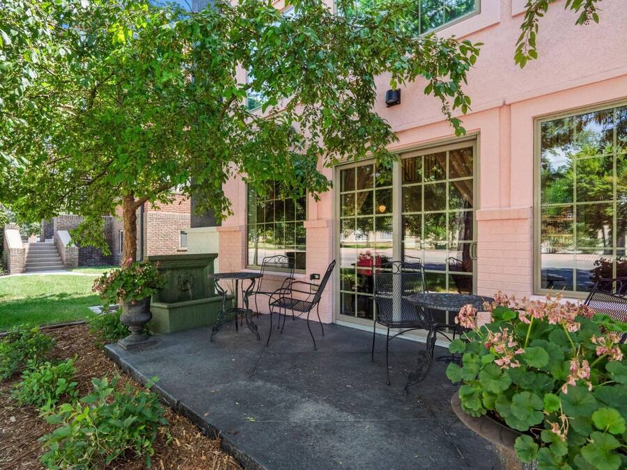 An outdoor patio with a table and chairs, a planter with flowers, and a building with large windows.