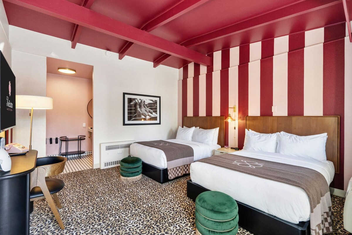 Une chambre d’hôtel avec deux lits, un bureau, une chaise, une lampe et un tableau encadré au mur.