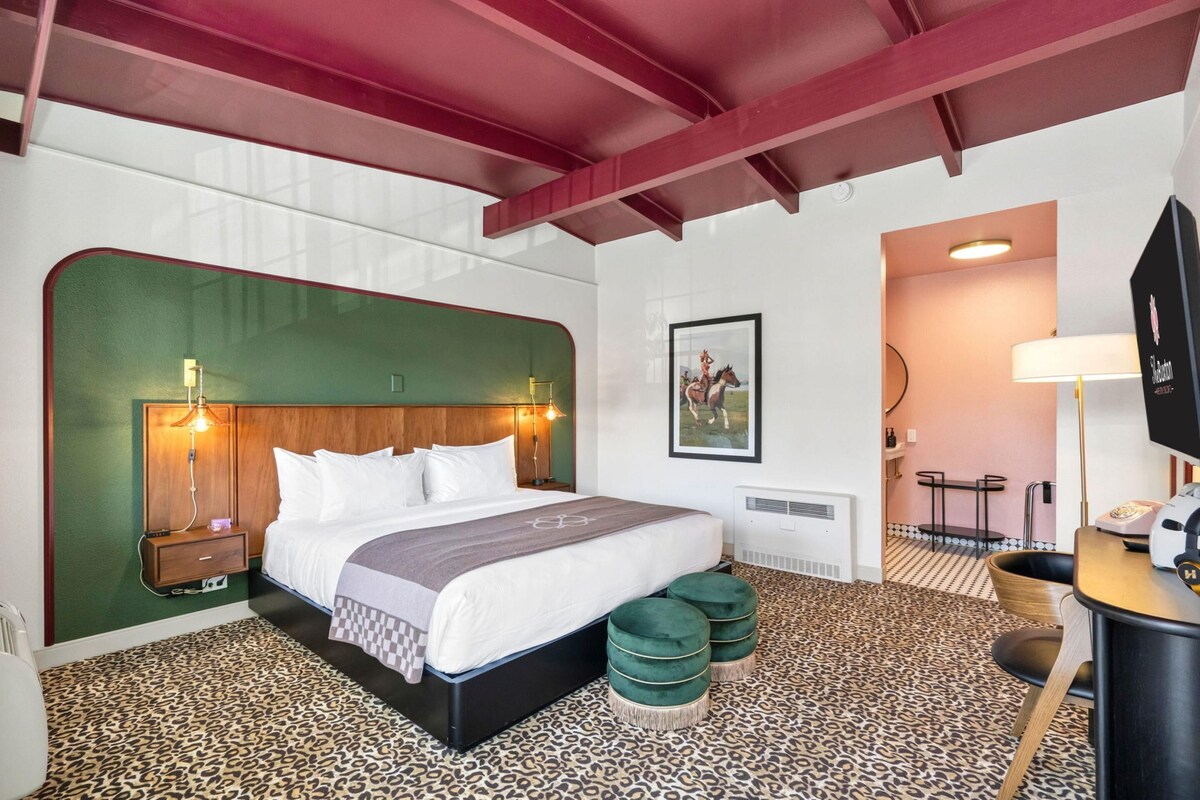 Une chambre d’hôtel avec un lit, des tables de chevet, un bureau, une chaise, un téléviseur et un tableau au mur.