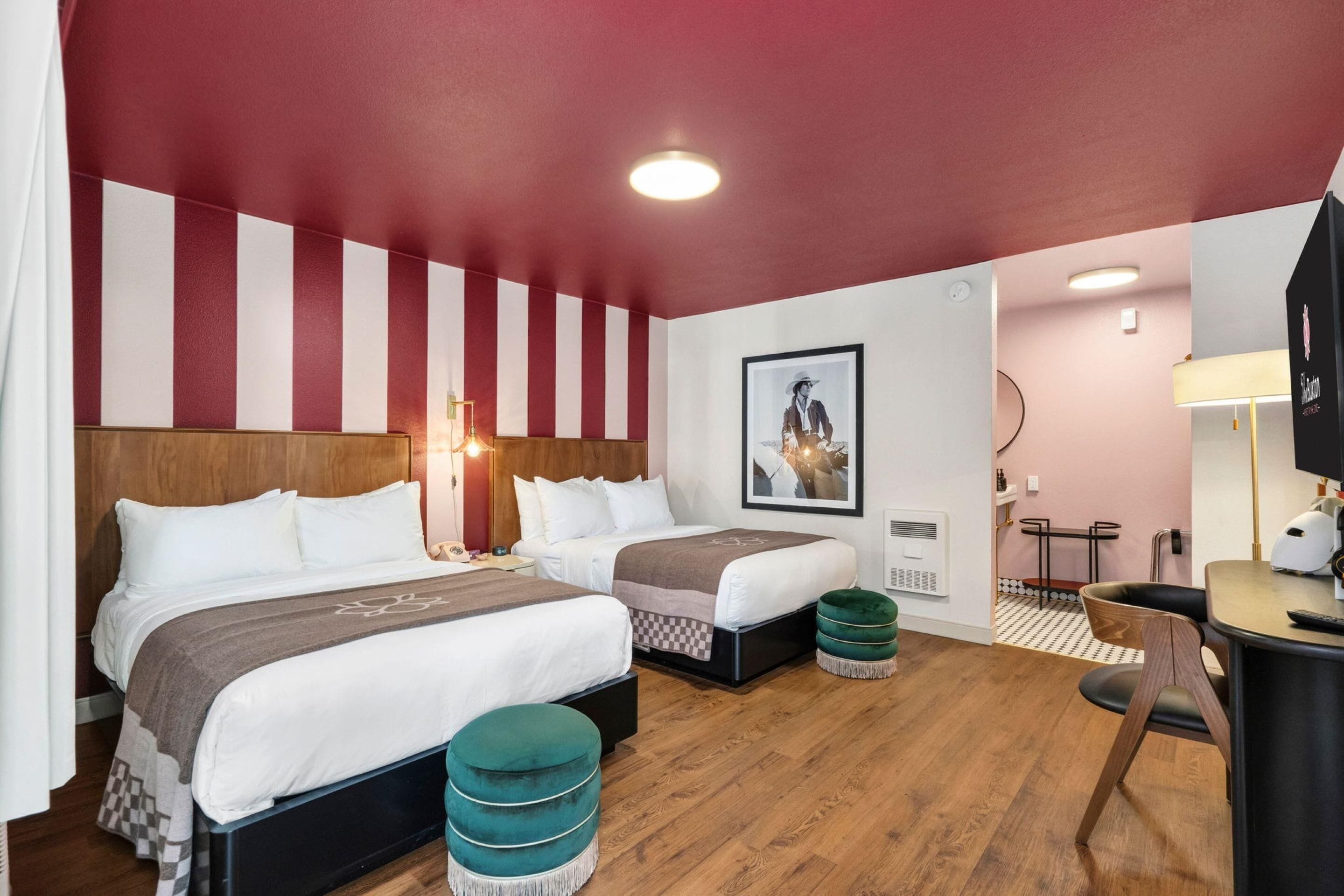 A hotel room with two beds, a desk, a chair, a small table, and a picture on the wall.