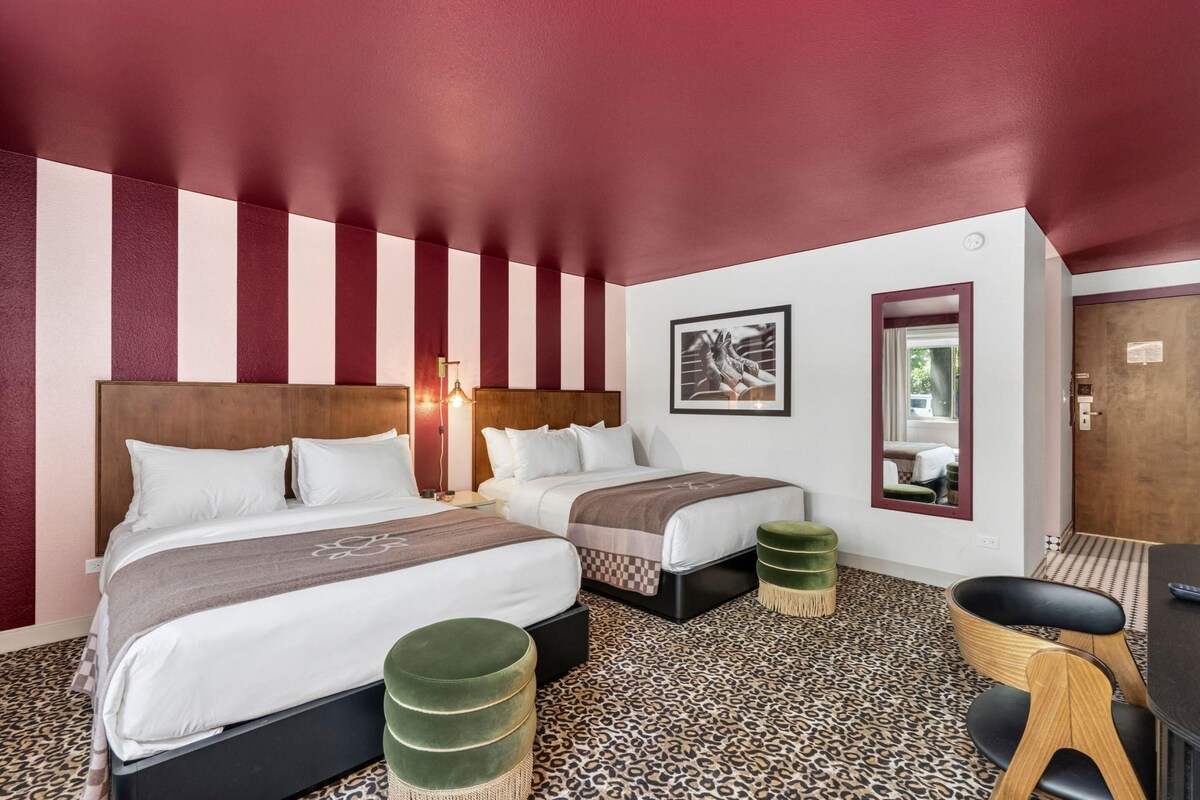 Une chambre d’hôtel avec deux lits, un bureau, une chaise et un tapis à motifs léopard.