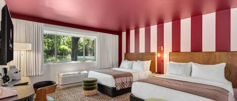 Una habitación de hotel con dos camas, un escritorio con computadora, una silla y un ventanal con cortinas.