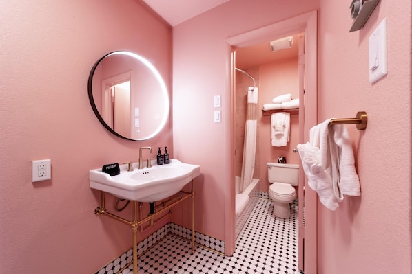 Ein Badezimmer mit einem weißen Waschbecken, einem runden Spiegel, einer Dusche und einer Toilette.