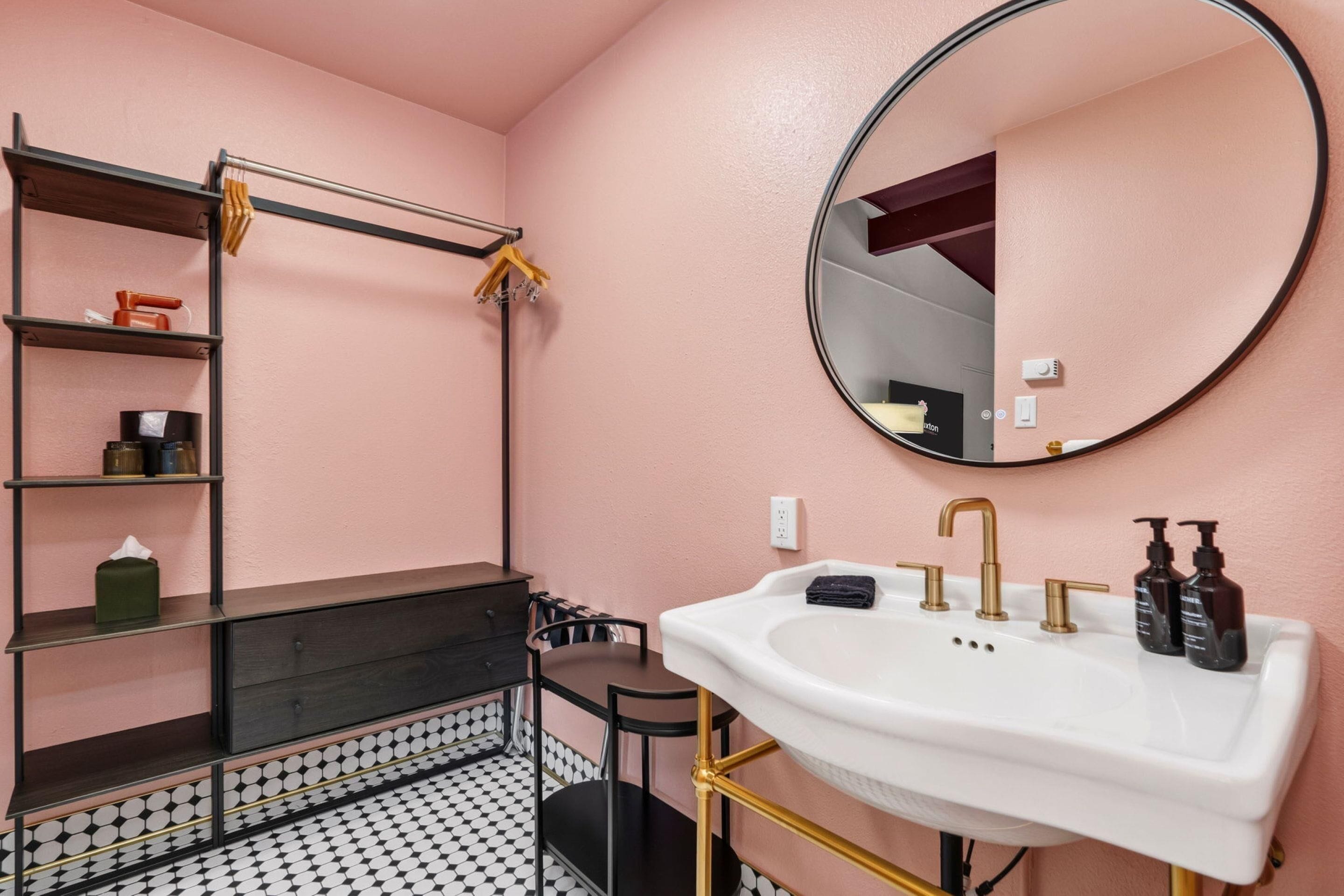 Ein Badezimmer mit einem weißen Waschbecken, goldenen Armaturen, einem runden Spiegel und einem schwarz-weißen Fliesenboden.