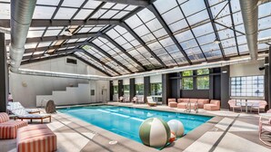 An indoor swimming pool with a glass ceiling, lounge chairs, and a view of the outdoors.