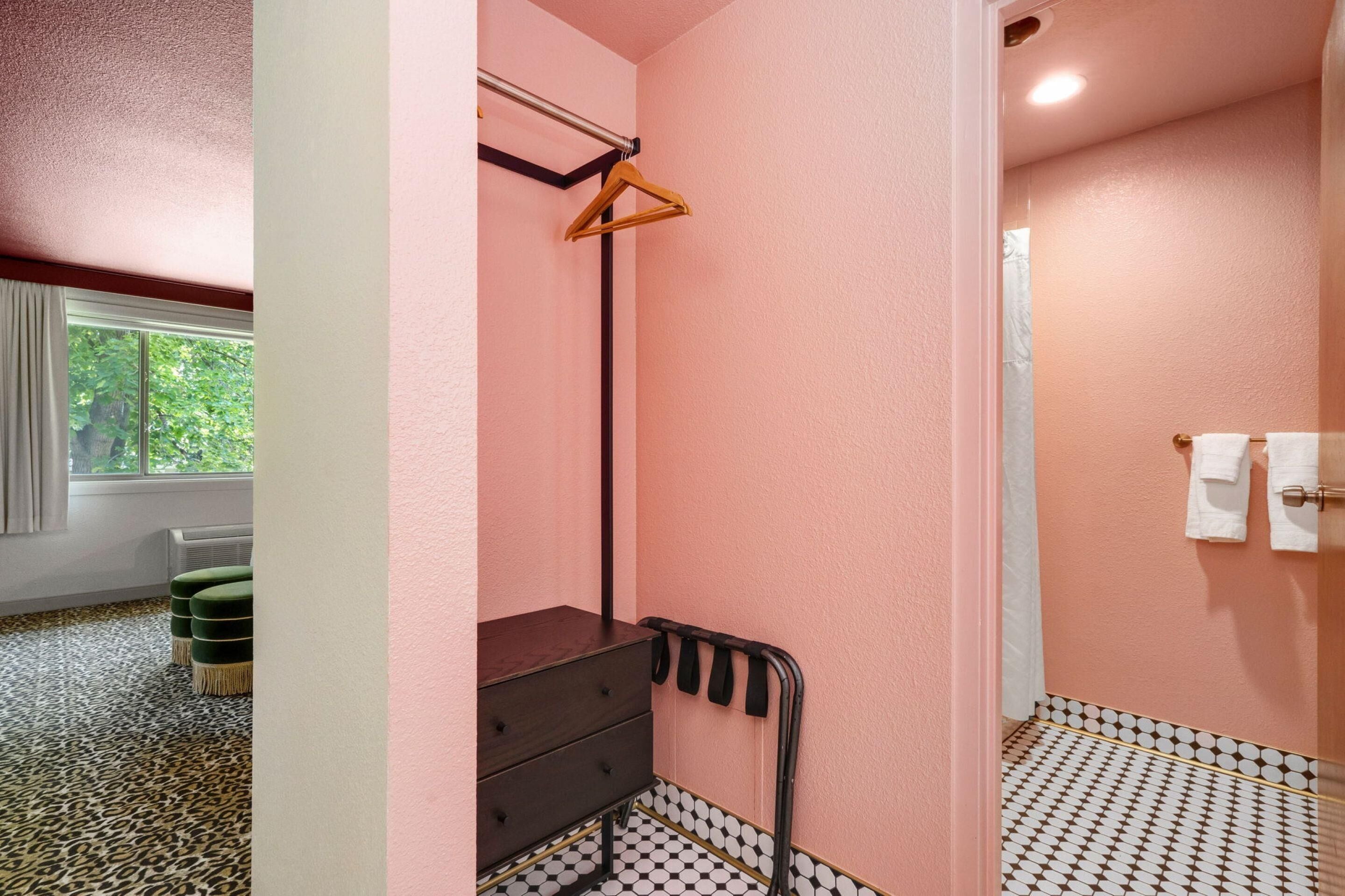 A bathroom with a pink wall, a black and white patterned floor, a wooden hanger rack, and a black metal towel rack.