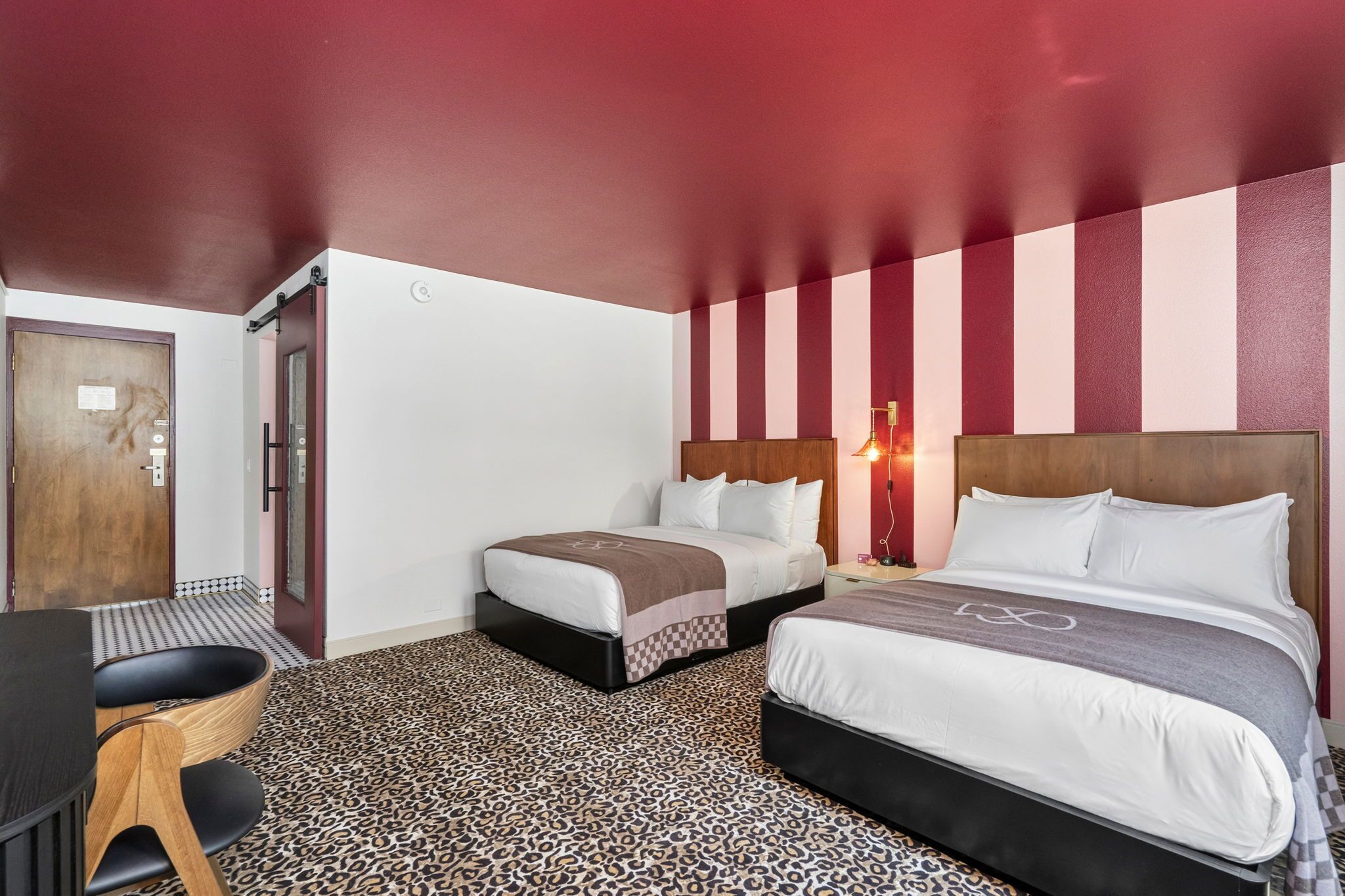 Une chambre d’hôtel avec deux lits, une porte en bois, une table avec des chaises et un tapis à motifs.