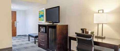 A hotel room with a bed, a desk with a chair, a television, a refrigerator, a microwave, a coffee maker, and a lamp.