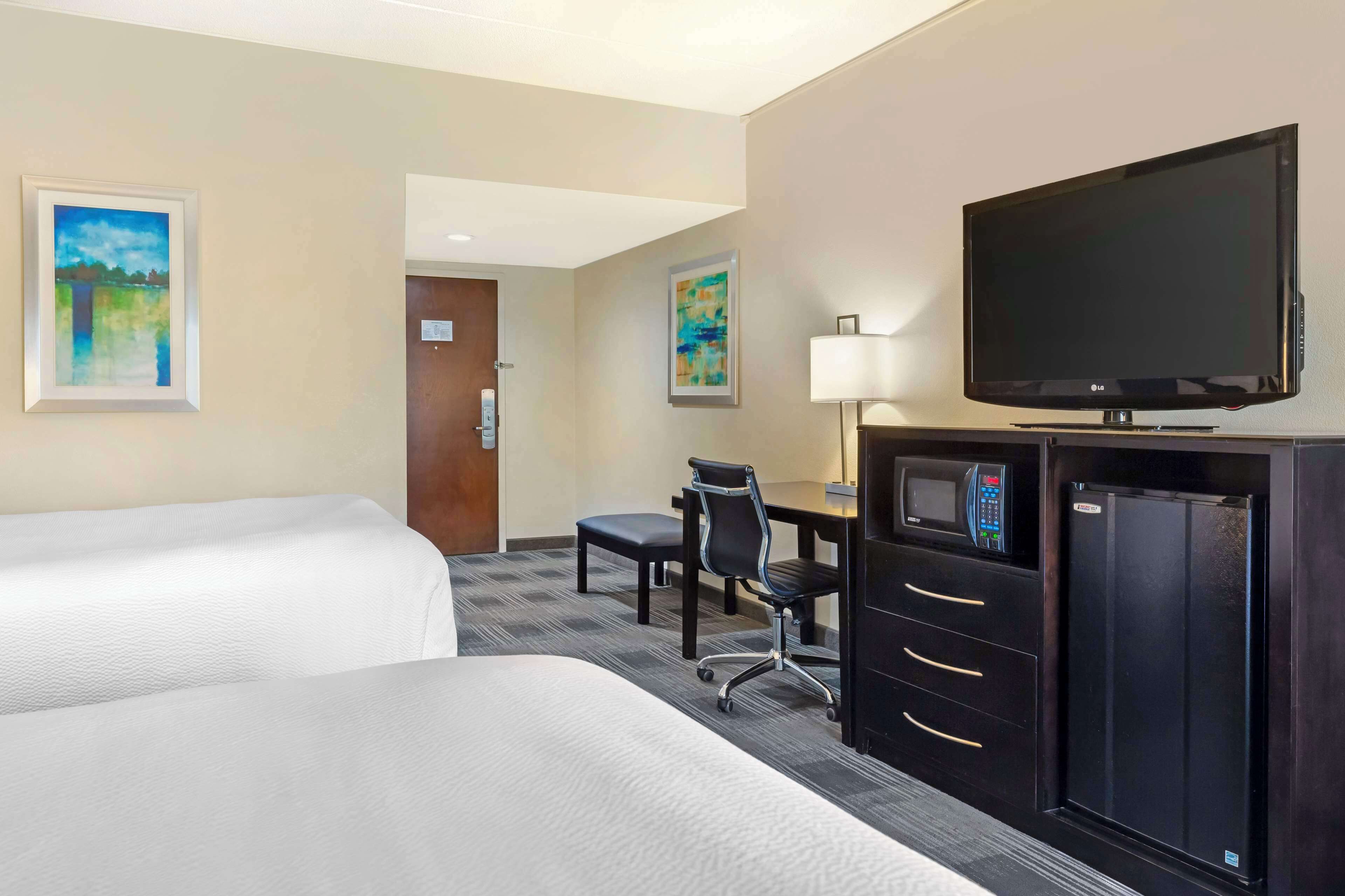 A hotel room with two beds, a desk with a chair, a television, and a refrigerator.