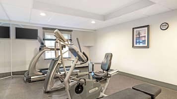 A fitness room with cardio equipment, a bench, and a wall-mounted TV.