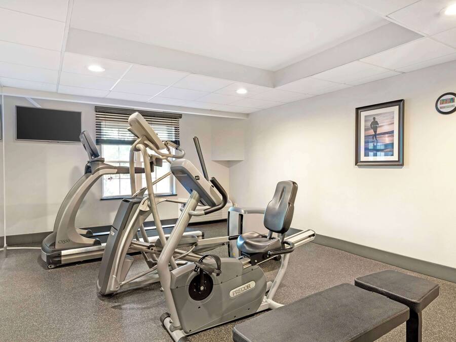 A fitness room with cardio equipment, a bench, and a wall-mounted TV.