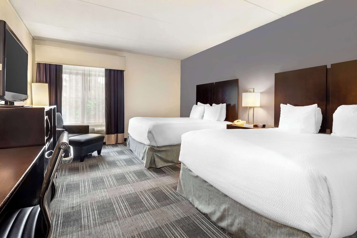 Ein Hotelzimmer mit zwei Betten, einem Schreibtisch mit Fernseher, einer Lampe und einem Fenster mit Vorhängen.
