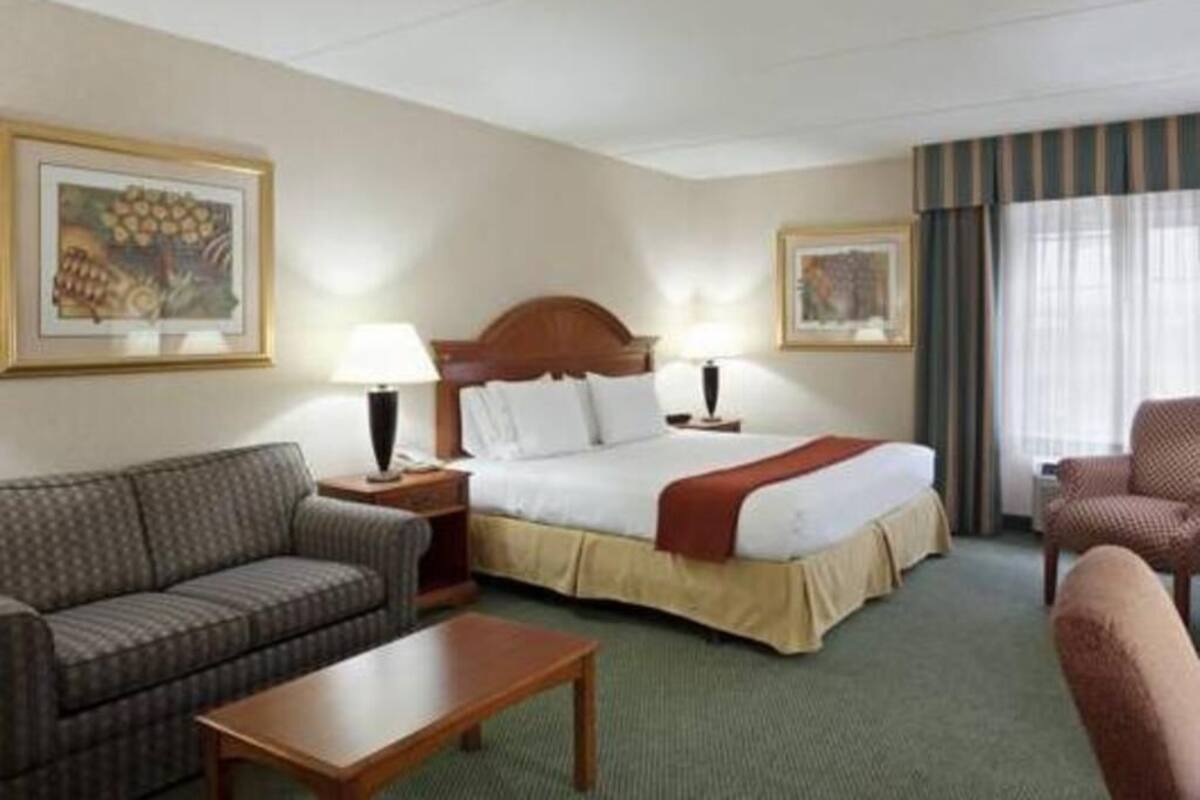 Ein Hotelzimmer mit einem Bett, zwei Nachttischen mit Lampen, einem Sofa, einem Sessel und zwei gerahmten Bildern an den Wänden.
